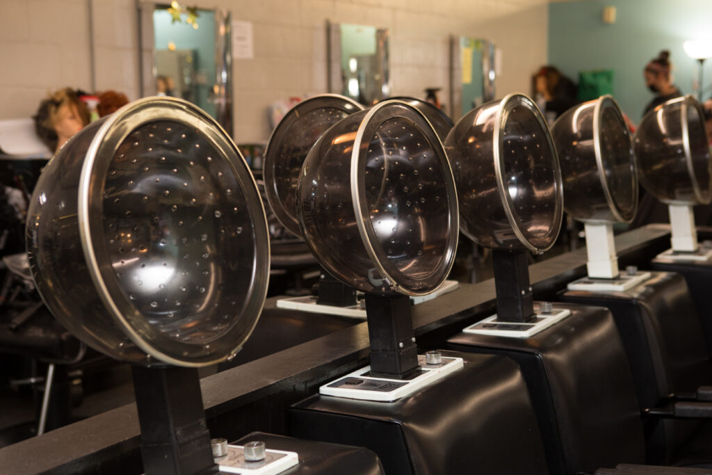 Four seated hair dryers in a row at Legrand Institute of Cosmetology